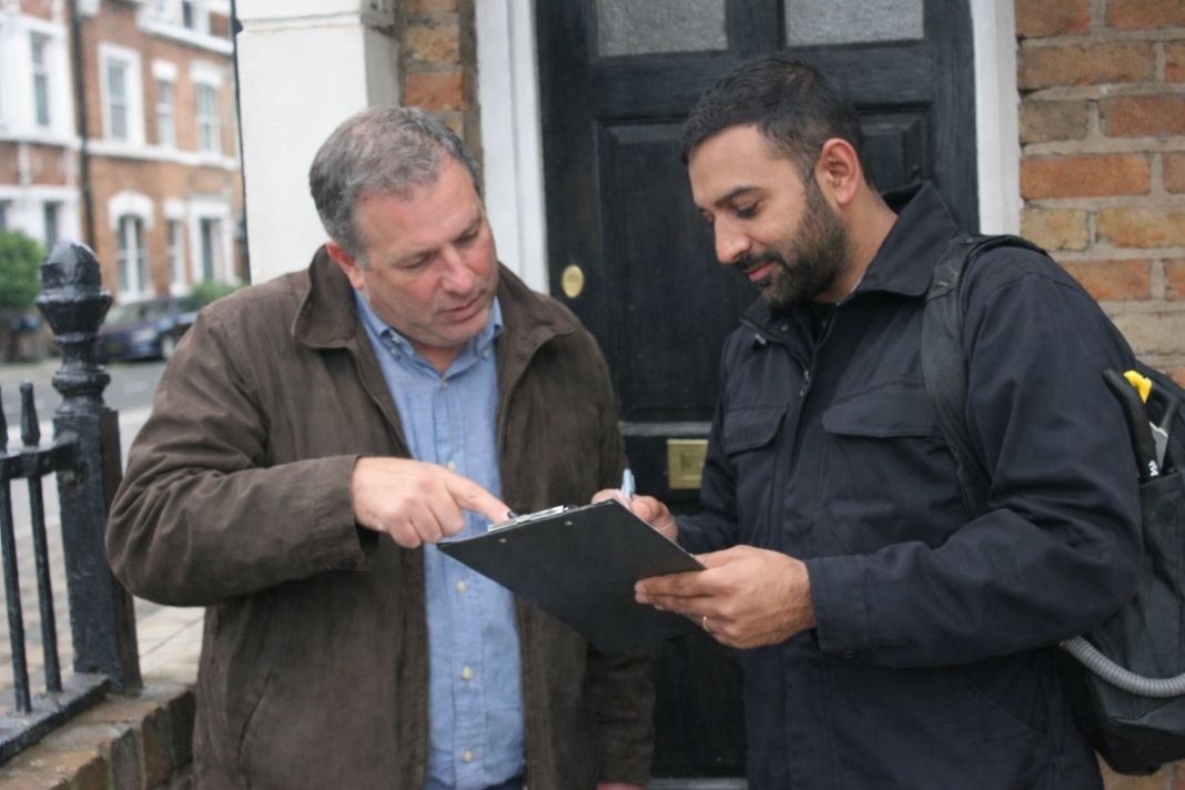 An illustrative image of a gas engineer discussing a checklist near the main entrance of a typical London flat