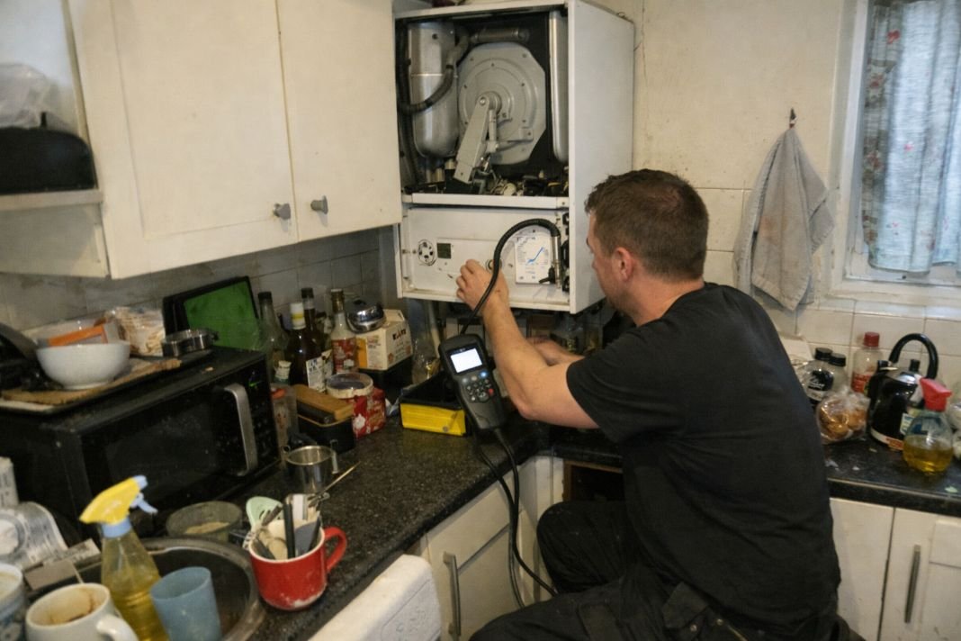 An illustrative image of a gas engineer testing a boiler in a cluttered London flat kitchen