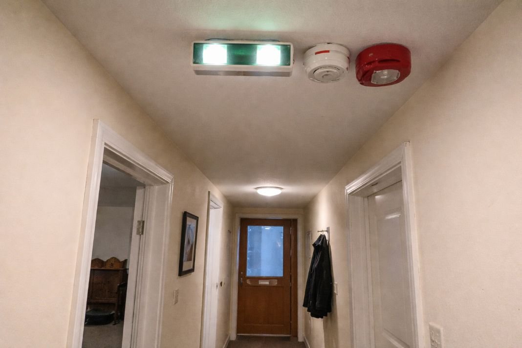 An illustrative image of a hallway in a shared house showing emergency lighting and fire alarm units on the ceiling