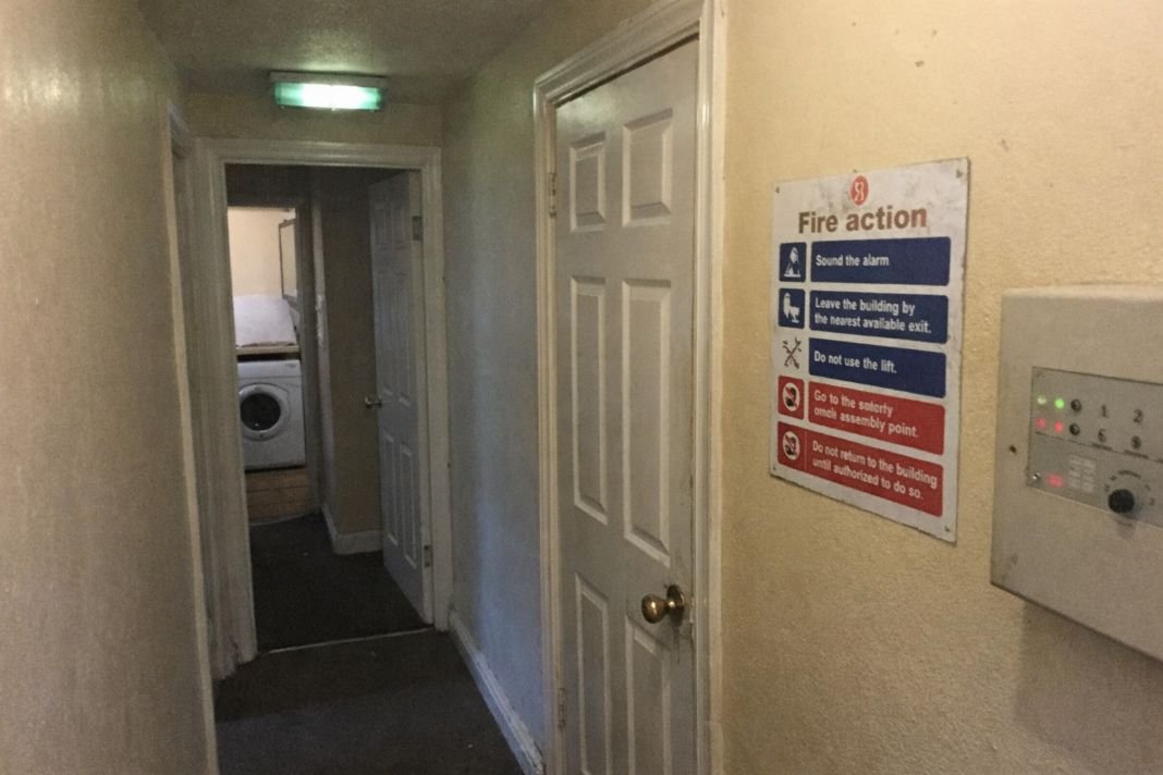 An illustrative image of a modest London HMO property hallway with fire safety sign and emergency lighting panel partly visible