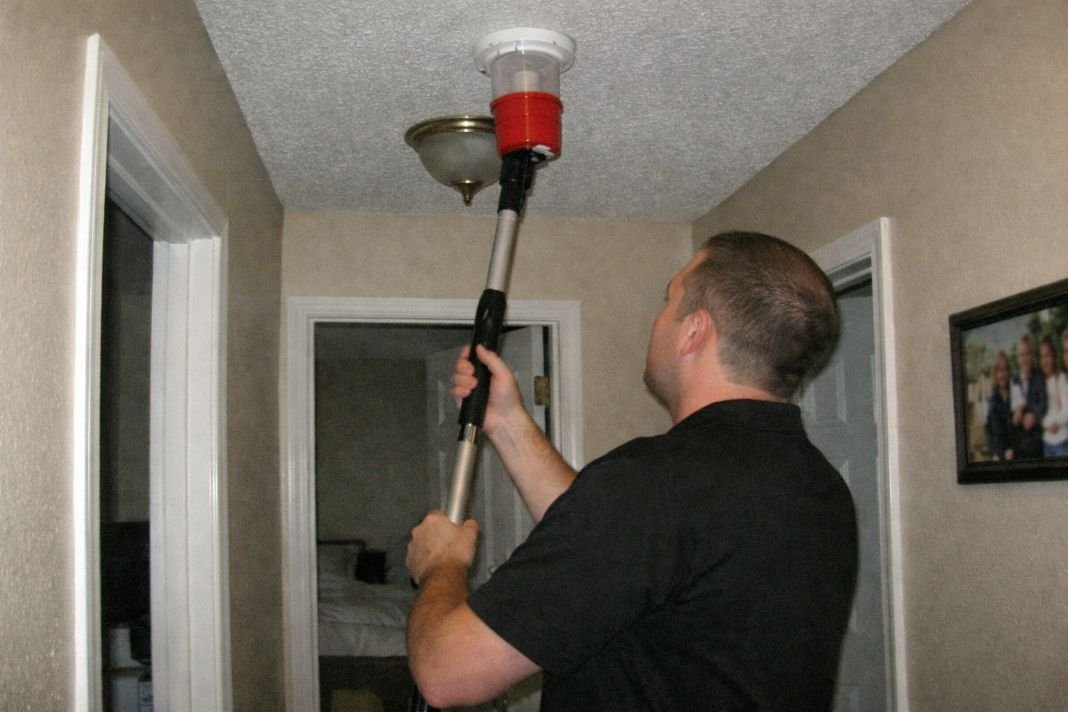 An illustrative image of a residential hallway where a fire alarm is being tested by a professional