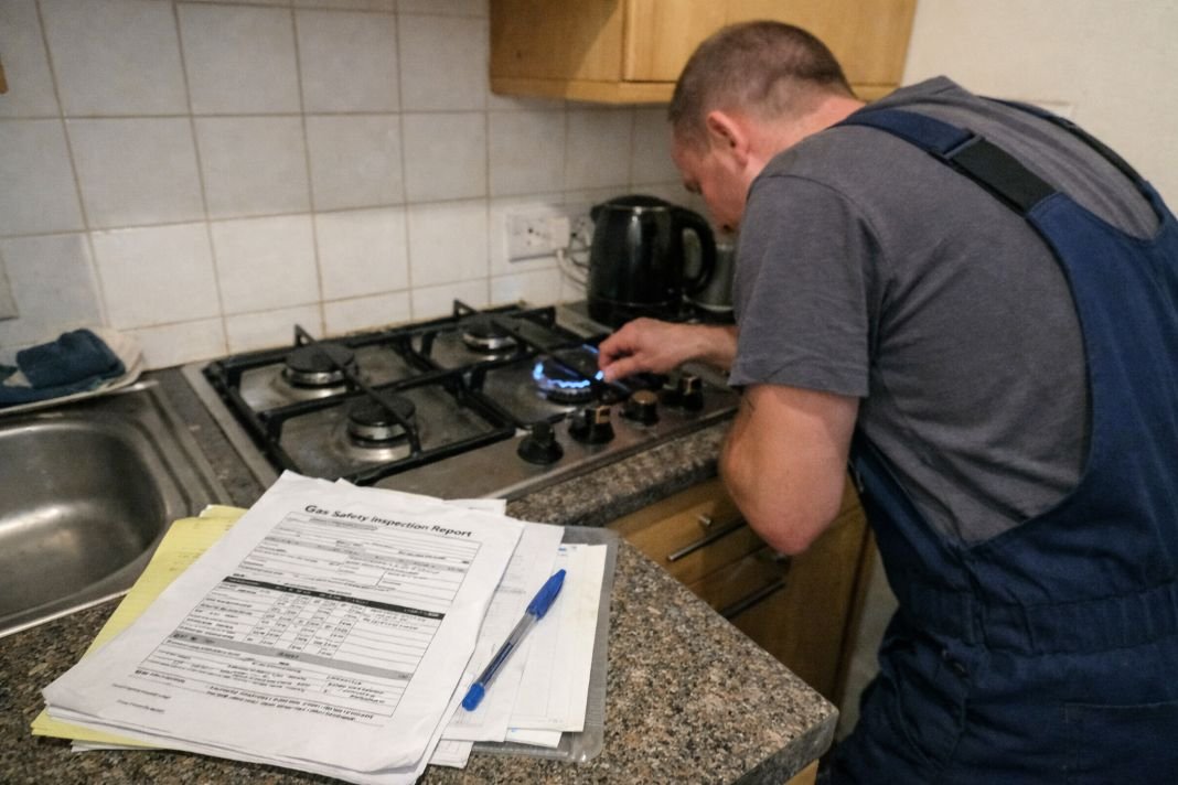 An illustrative image of a small kitchen in a rental flat with a gas hob being inspected by a technician