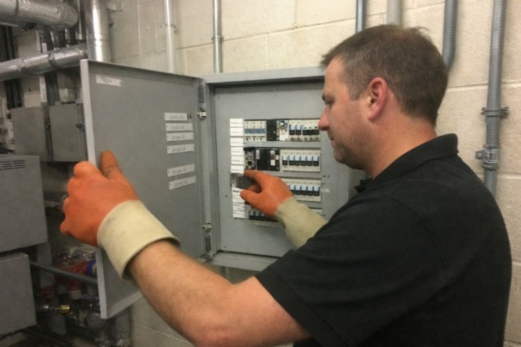An illustrative image of an electrician checking a distribution board in a well-lit plant room