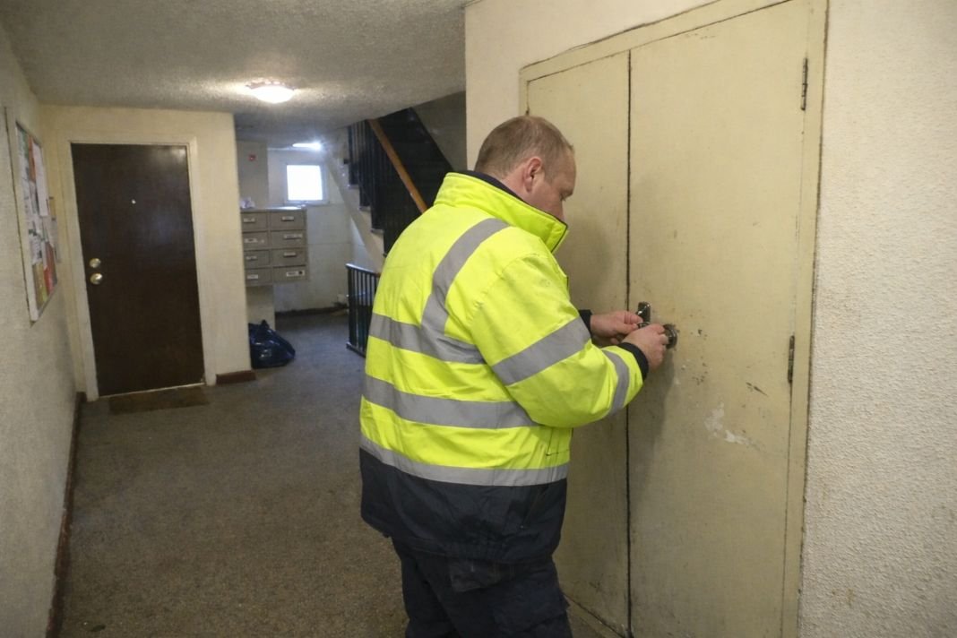 An illustrative image of of a small block of London rental flats with an engineer unlocking a utility cupboard