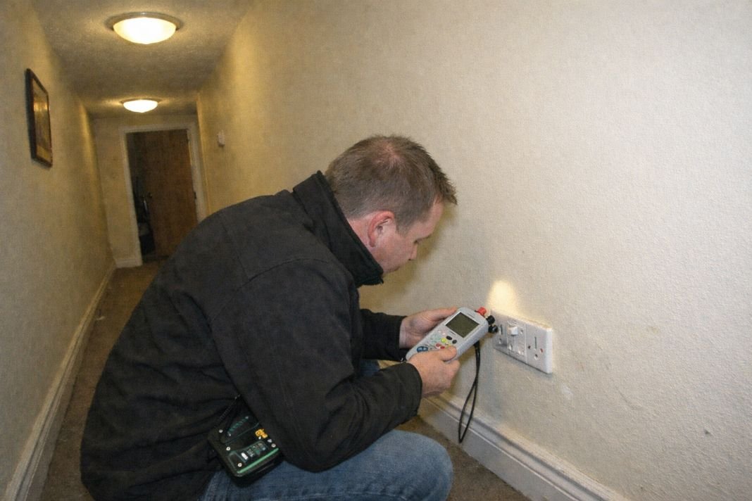 An illustrative image of a hallway with visible light fittings and uk plug sockets being visually inspected