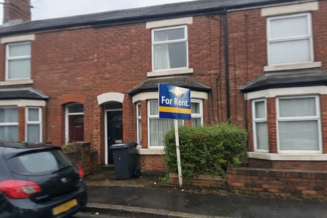 An illustrative image of a terraced rental property on a typical UK street with a for rent sign visible